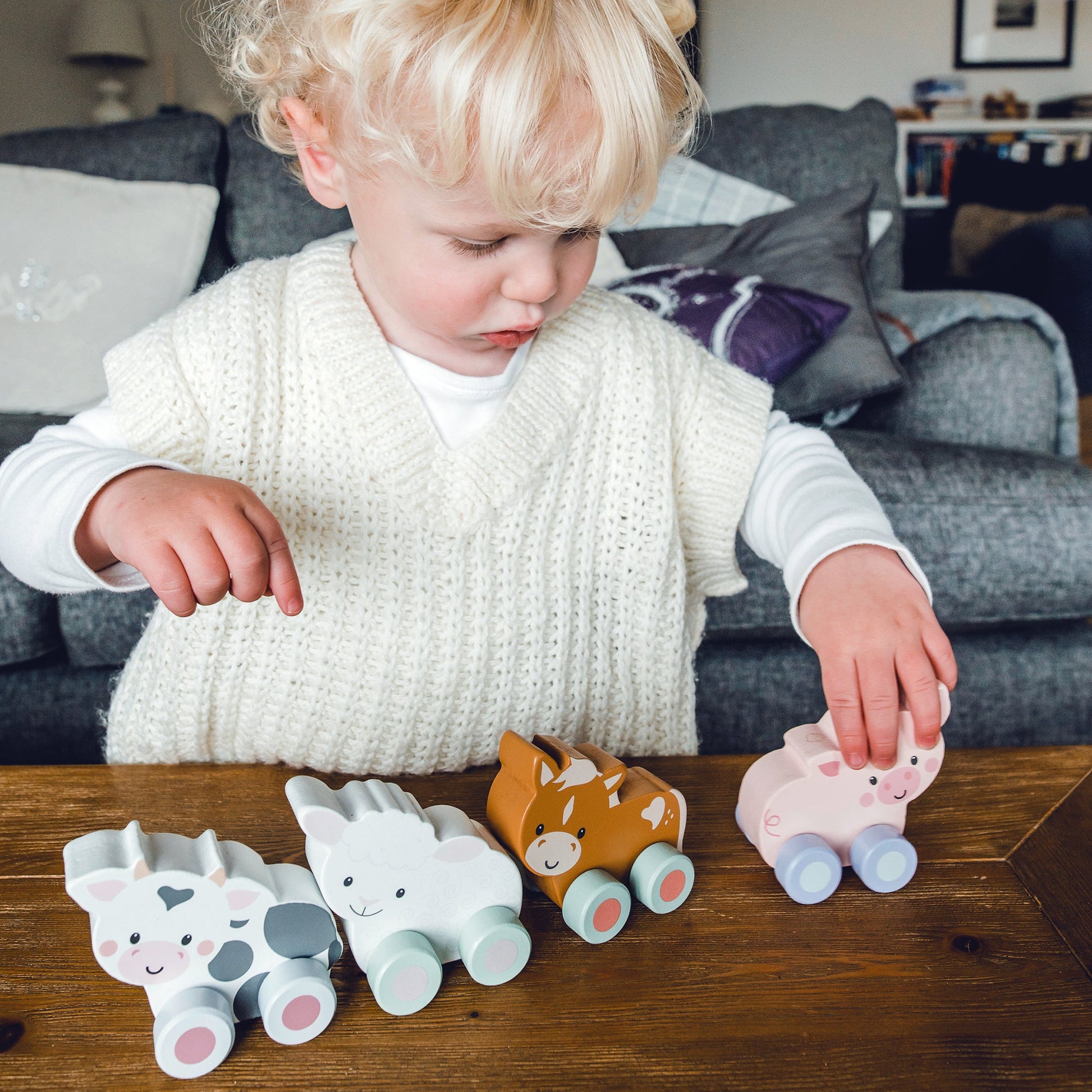 Toddler playing with a row of wooden farm animal push toys on a table