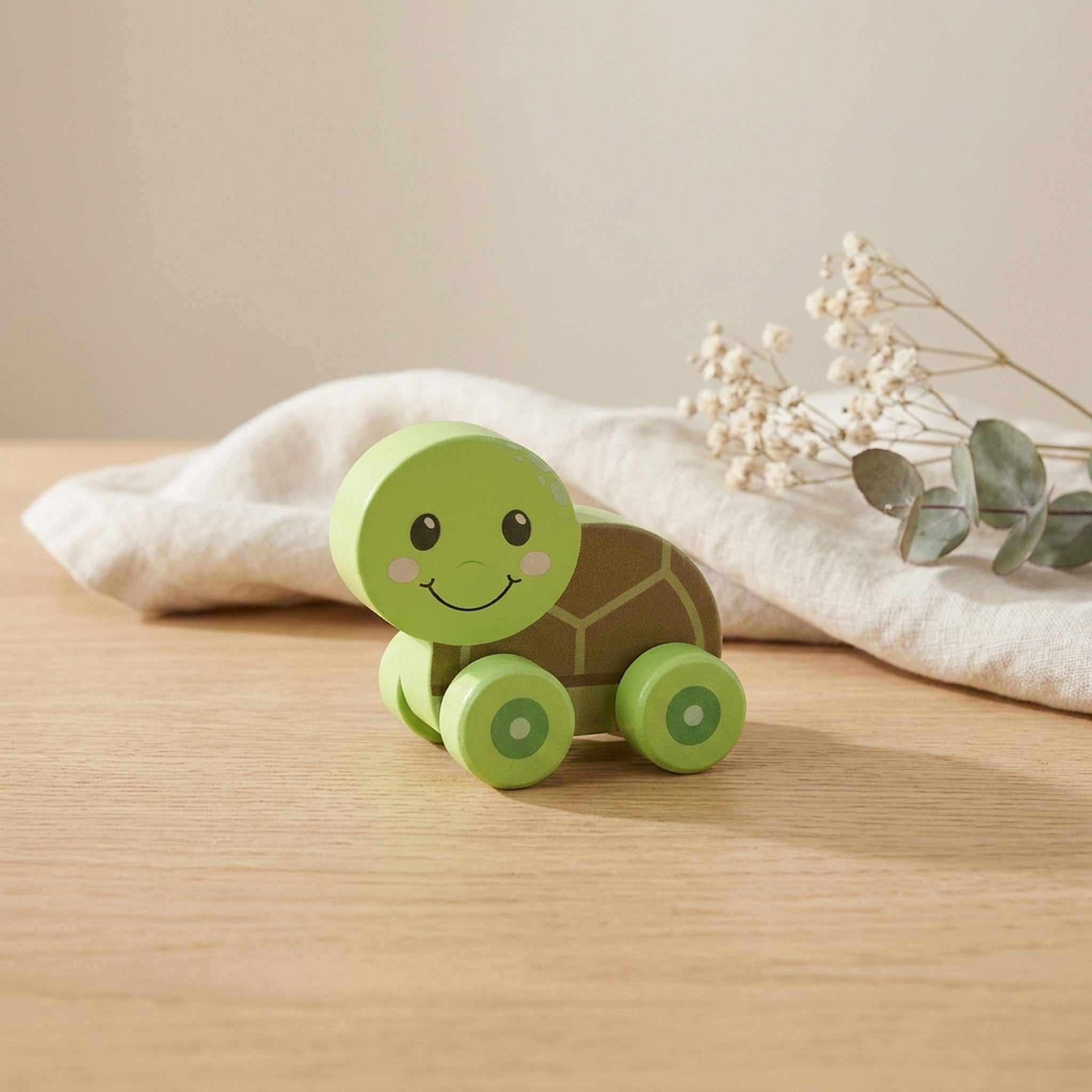 Green wooden turtle push toy on a warm oak table with cream linen and dried flowers