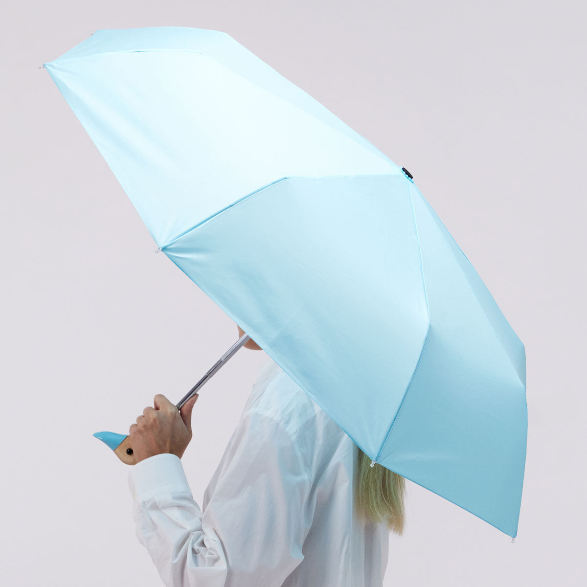 Popsicle blue duck umbrella open held by model side view on pink-grey background