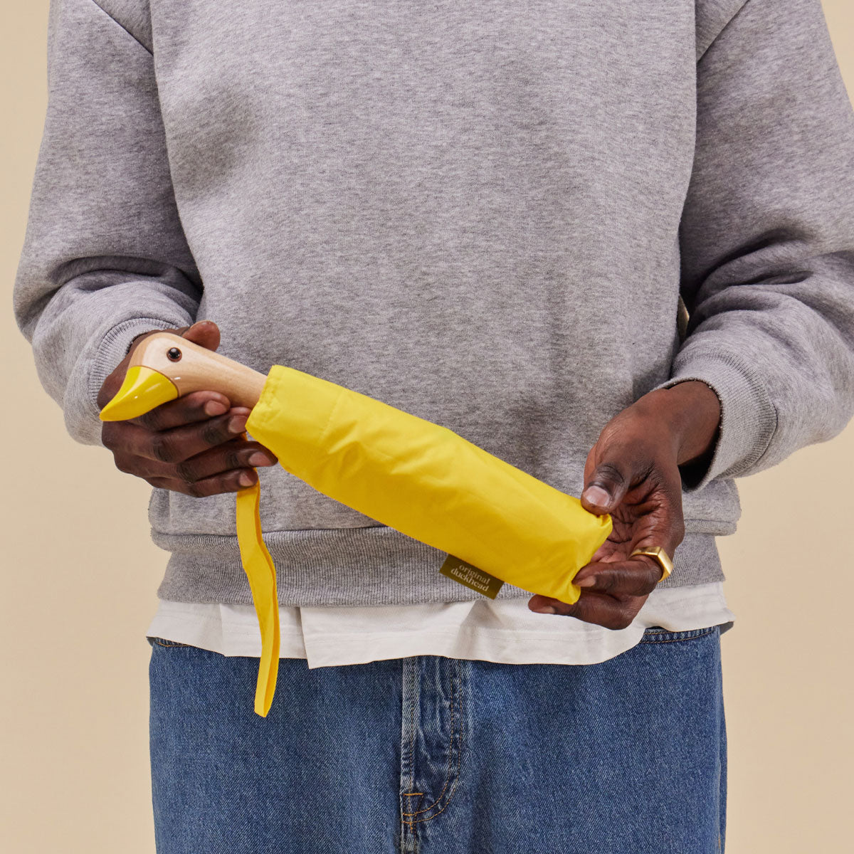 Closed yellow duck umbrella held in hands lifestyle on warm beige background