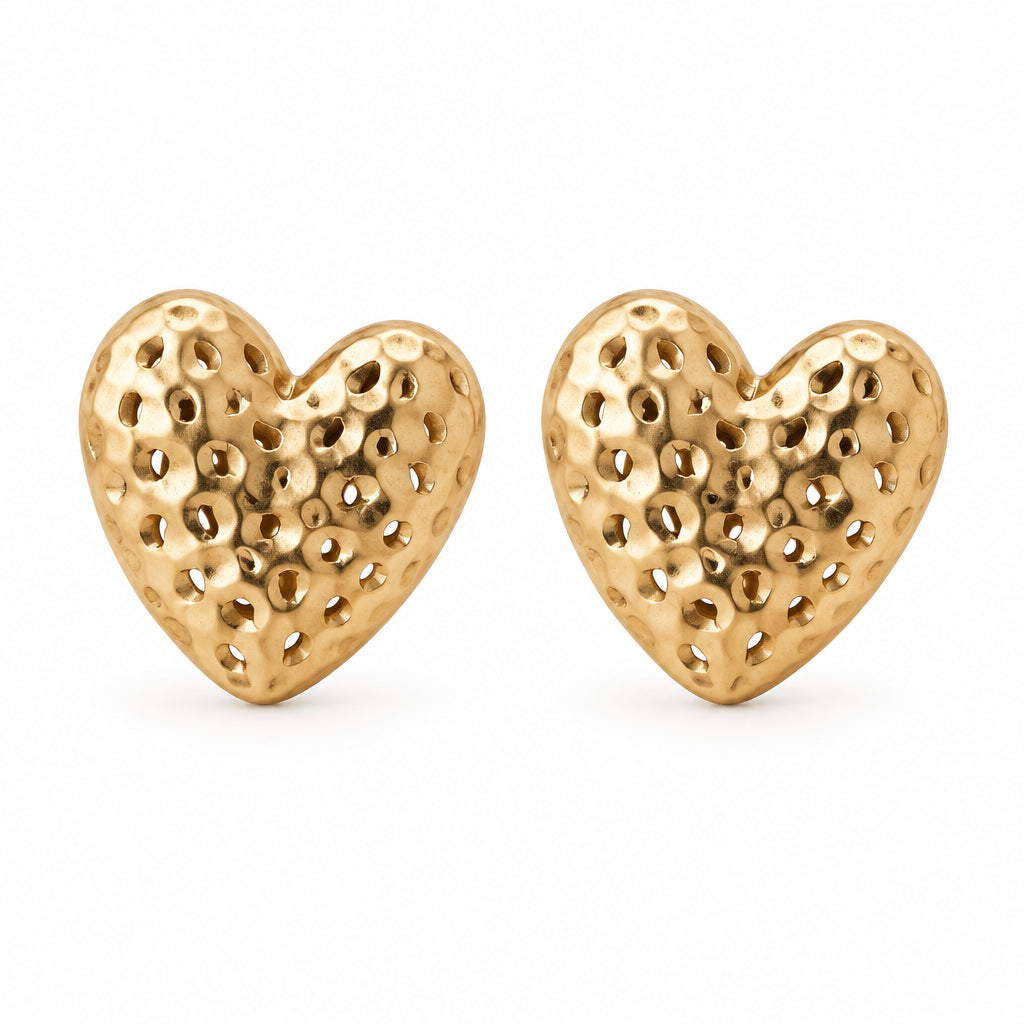 Gold hammered heart stud earrings beside a white dish on cream