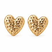 Gold hammered heart stud earrings beside a white dish on cream