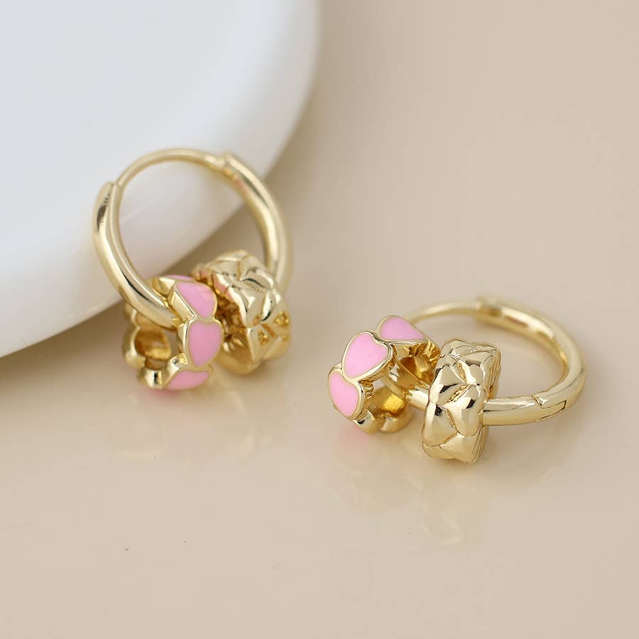 Pink enamel heart ring hoop earrings beside a white dish on cream