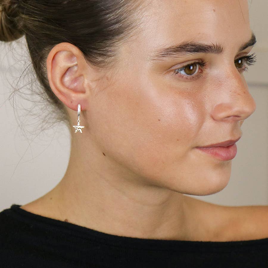 Silver hoop gold star earring worn by a woman with hair tied back
