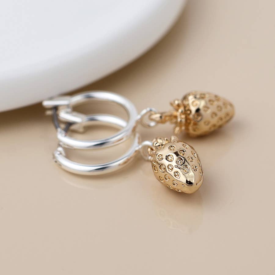 Silver hoop earrings with gold strawberry charms on a cream surface