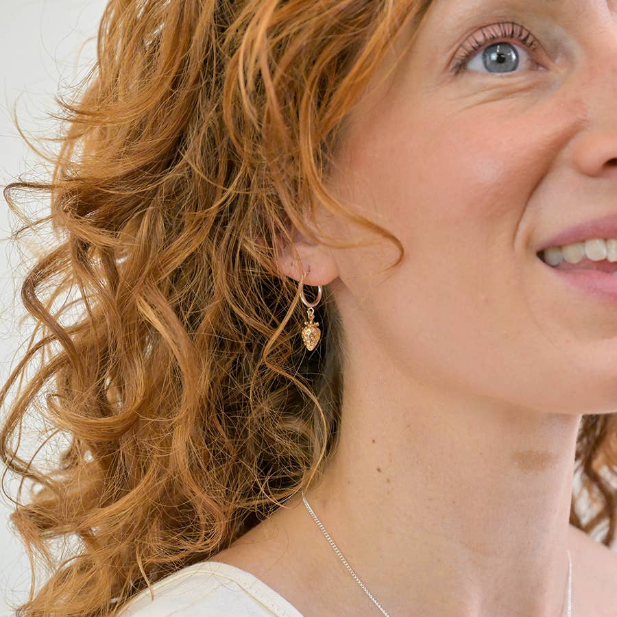 Silver hoop strawberry earring worn with curly auburn hair
