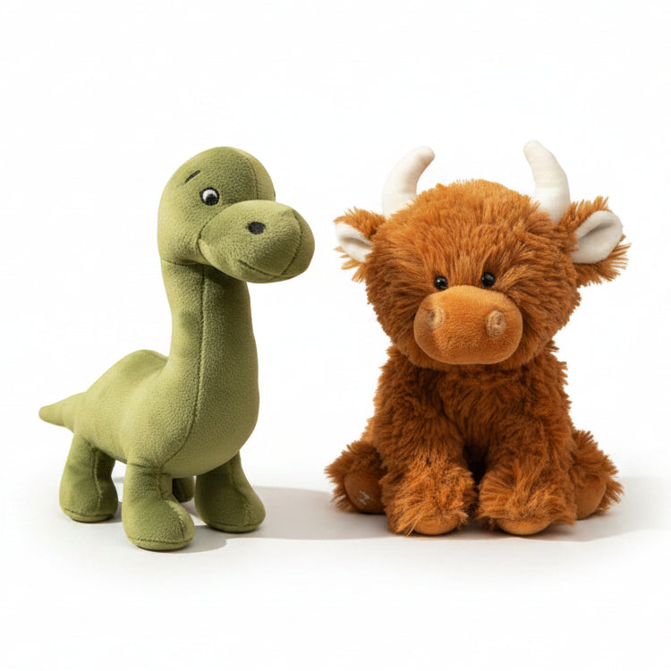 Two plush stuffed toys on a draped cream fabric backdrop: a green long-neck dinosaur on the left and a fluffy brown highland cow with white horns on the right.