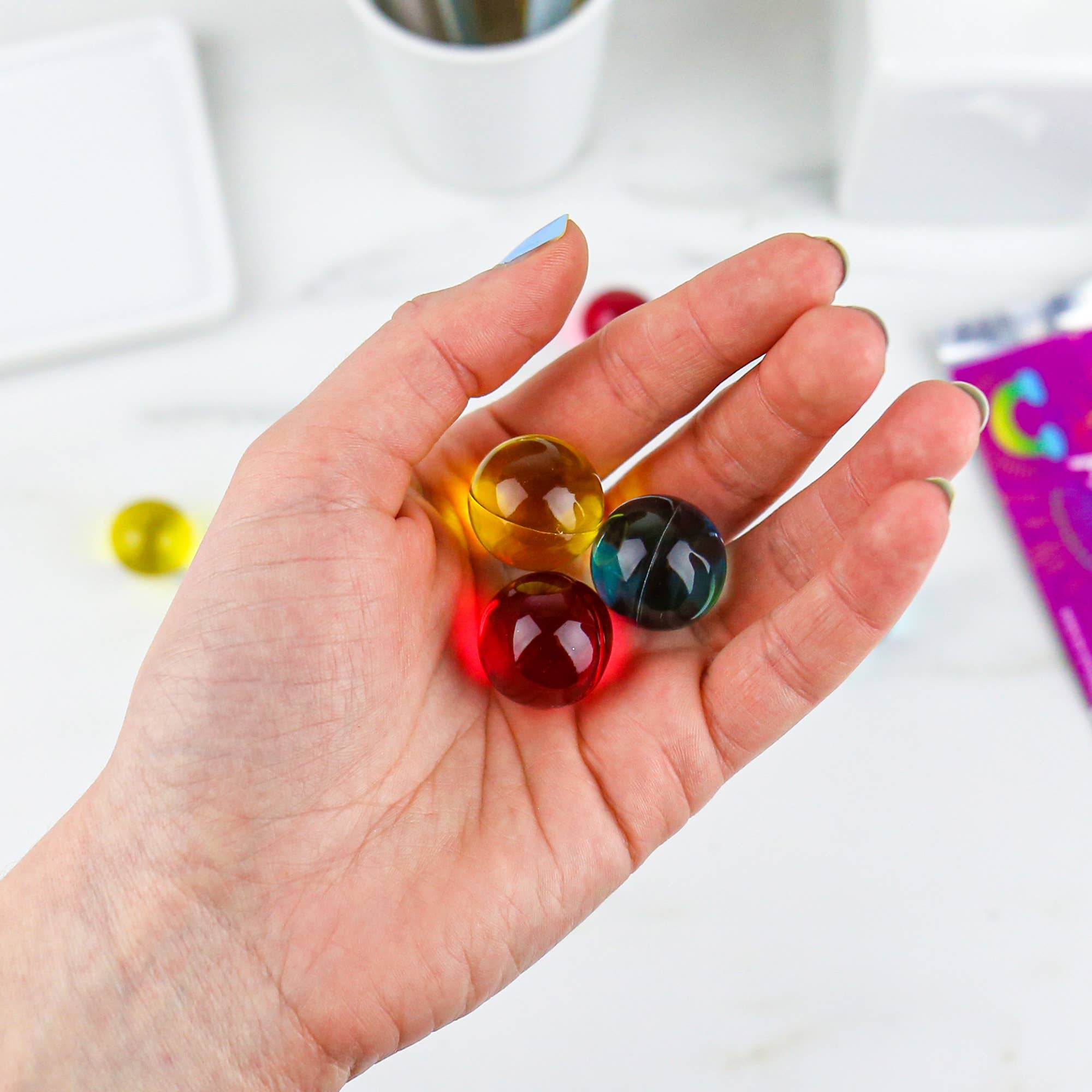 Hand holding three colourful rainbow bath pearls showing glossy texture.