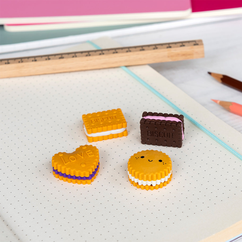 Four biscuit-shaped erasers on a dotted notebook beside ruler and pencils