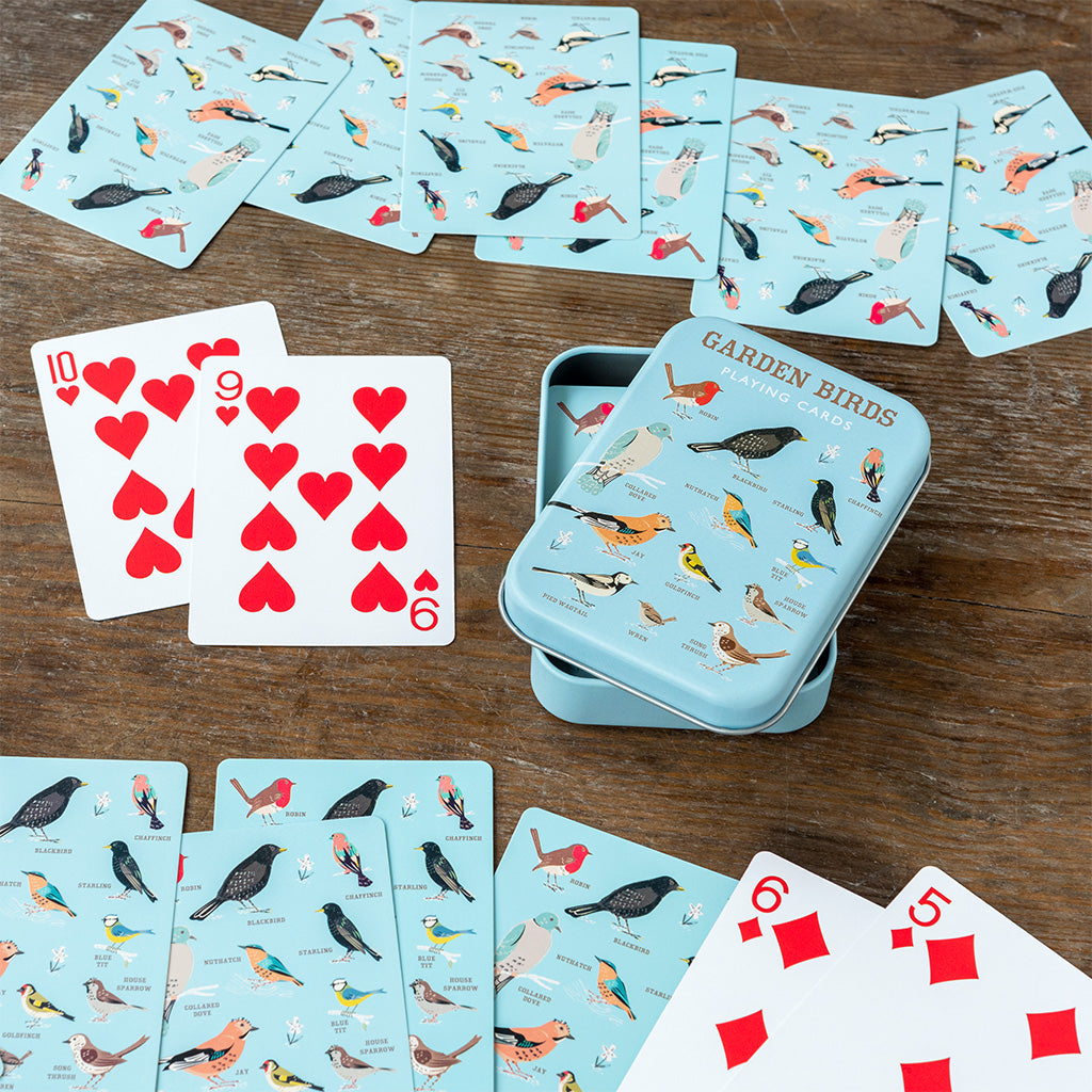 Garden Birds playing cards spread across a wooden table beside the open tin