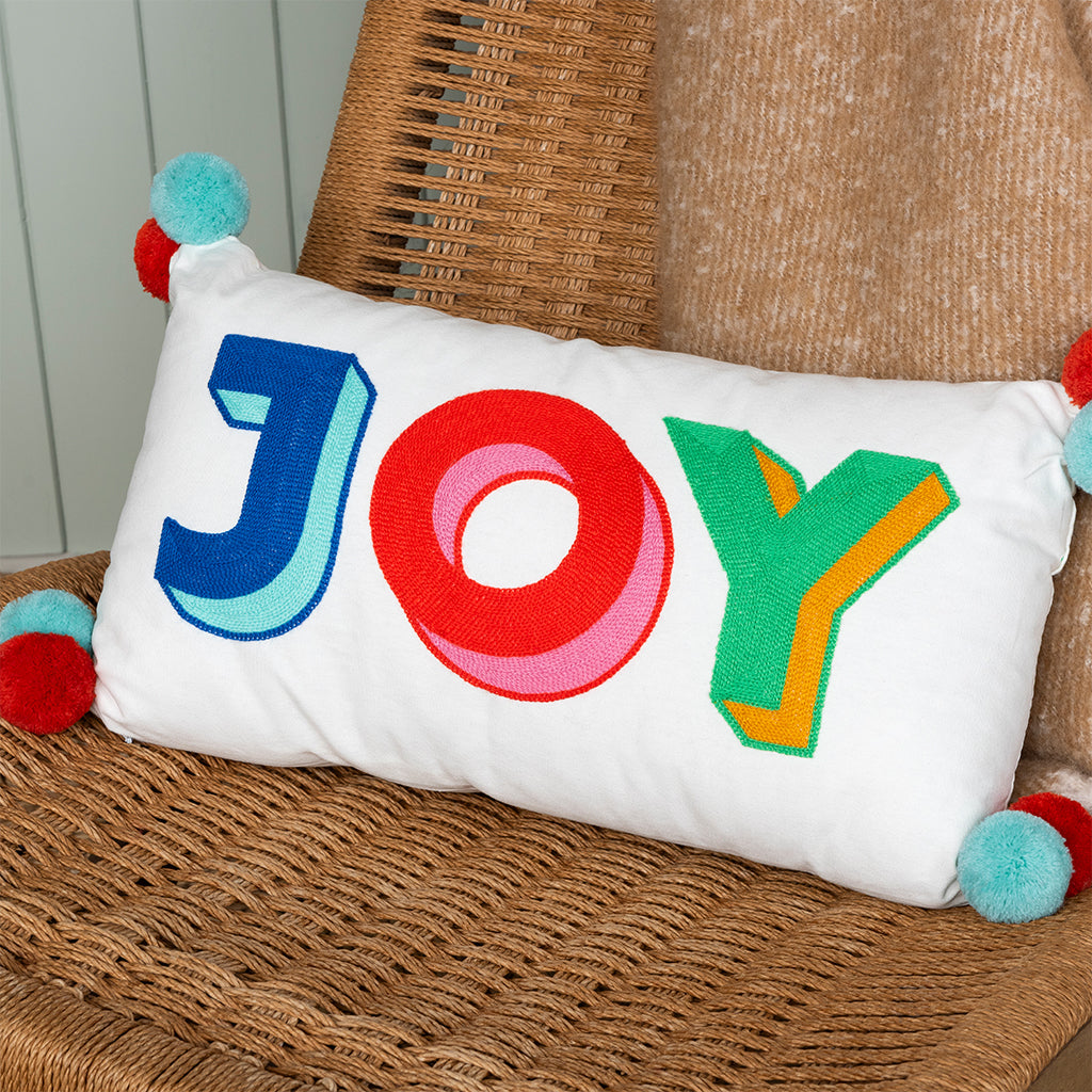 Joy embroidered cushion with pom poms on wicker chair