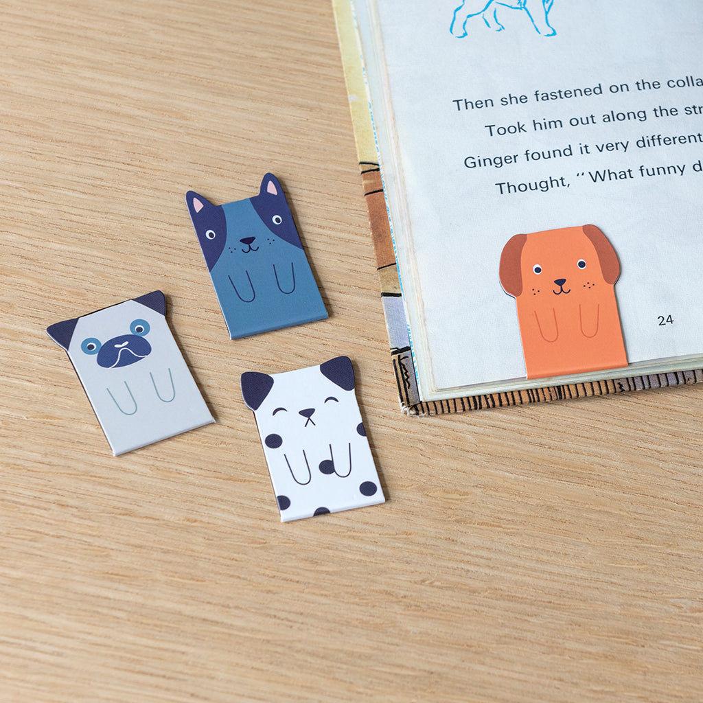 Magnetic dog bookmarks clipped to the pages of an open book on a wooden table
