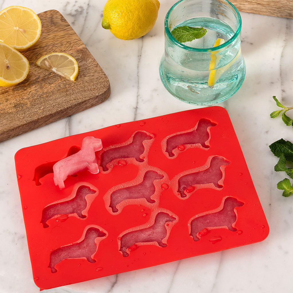Sausage dog ice cube tray on a board beside a glass of iced drink