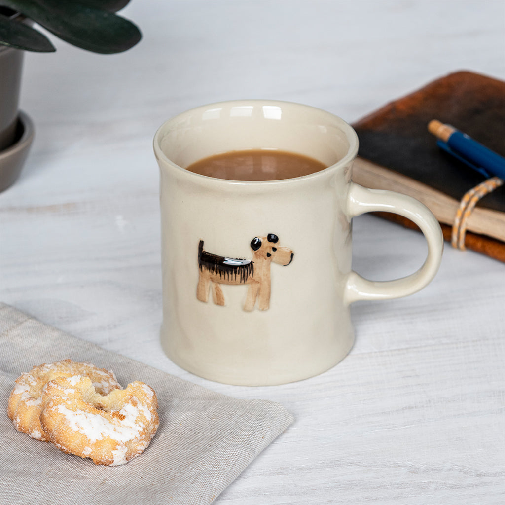 Cream dog mug filled with tea next to a pastry and a notebook