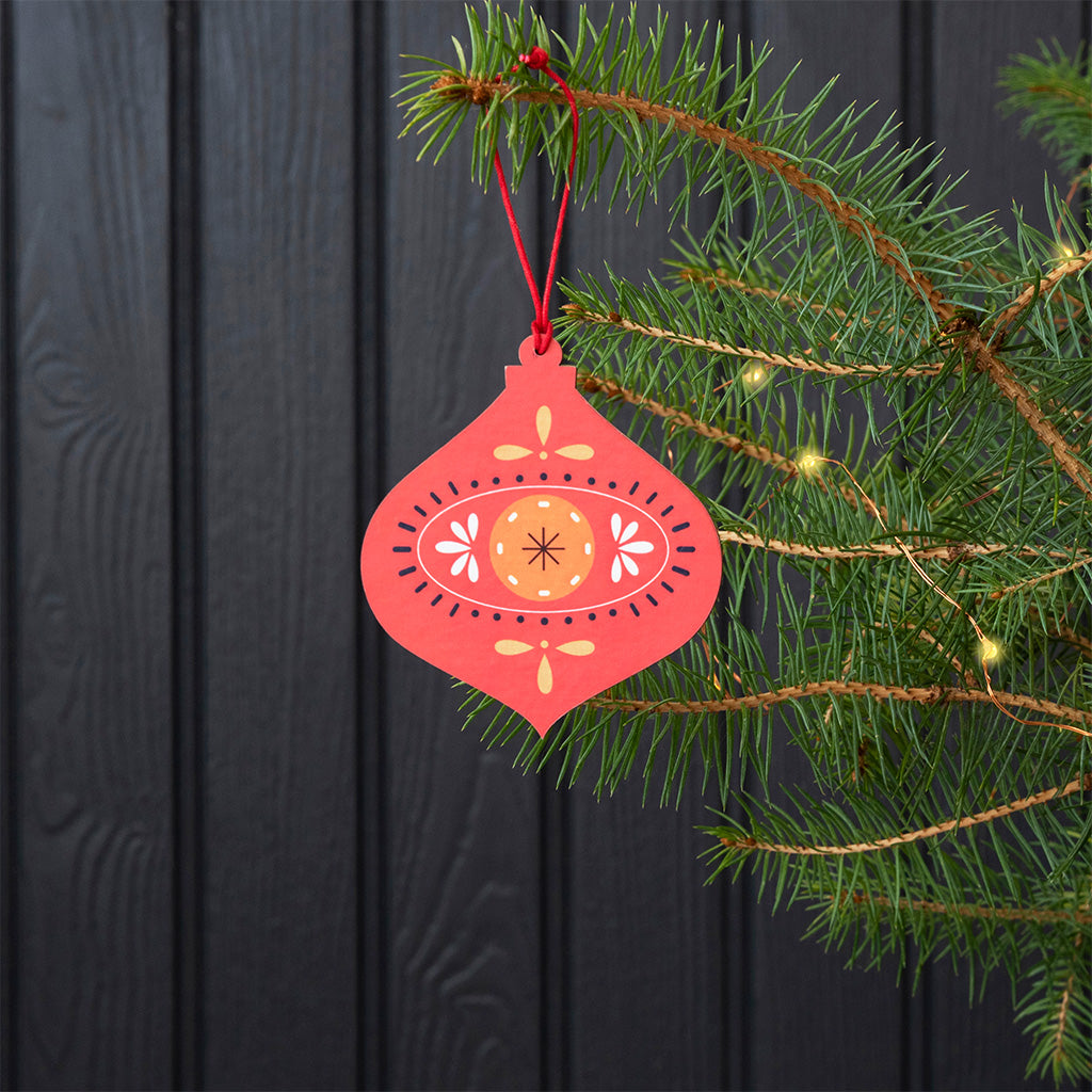 Red wooden bauble hanging from a Christmas tree branch beside fairy lights
