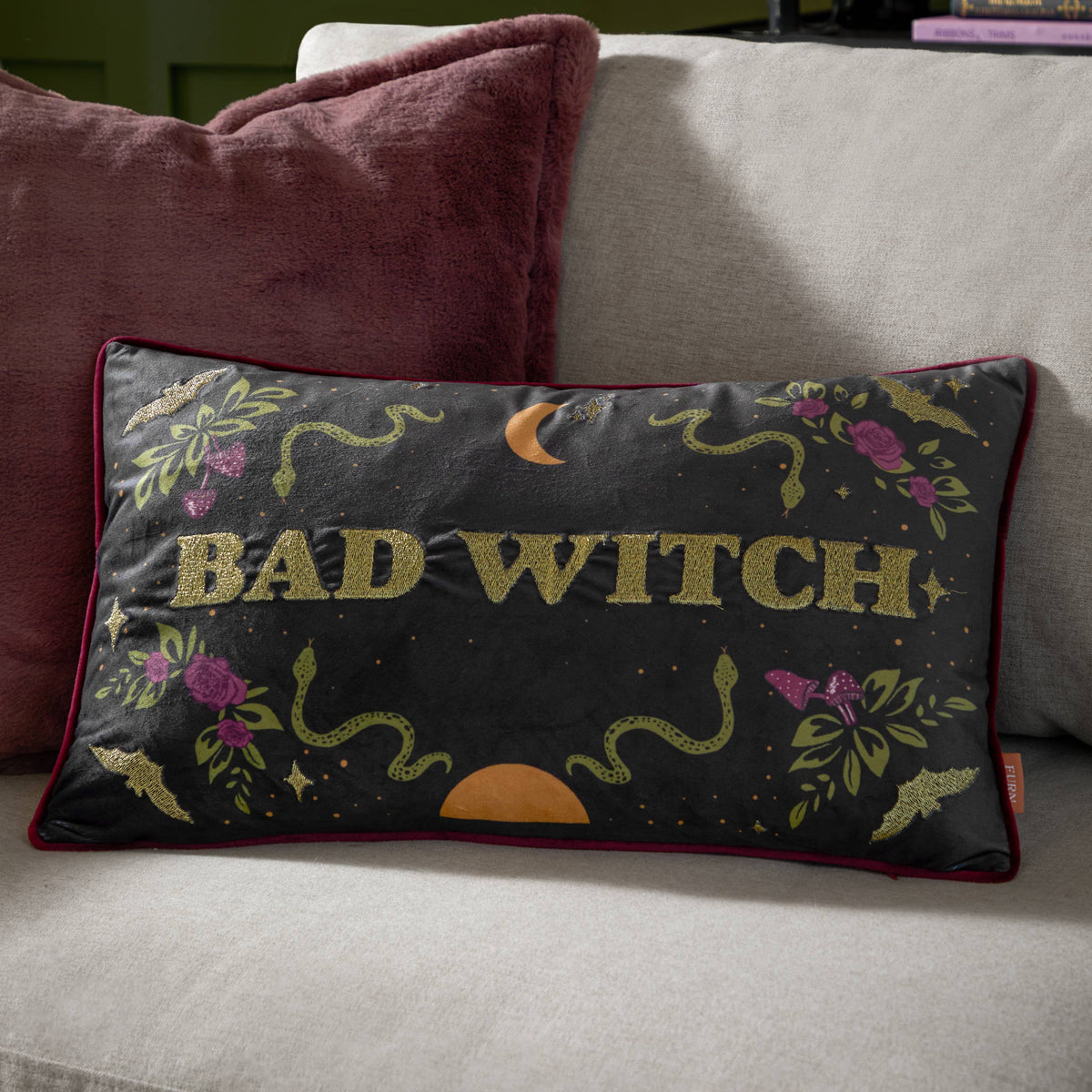 Bad Witch cushion styled on a cream sofa with a berry velvet cushion