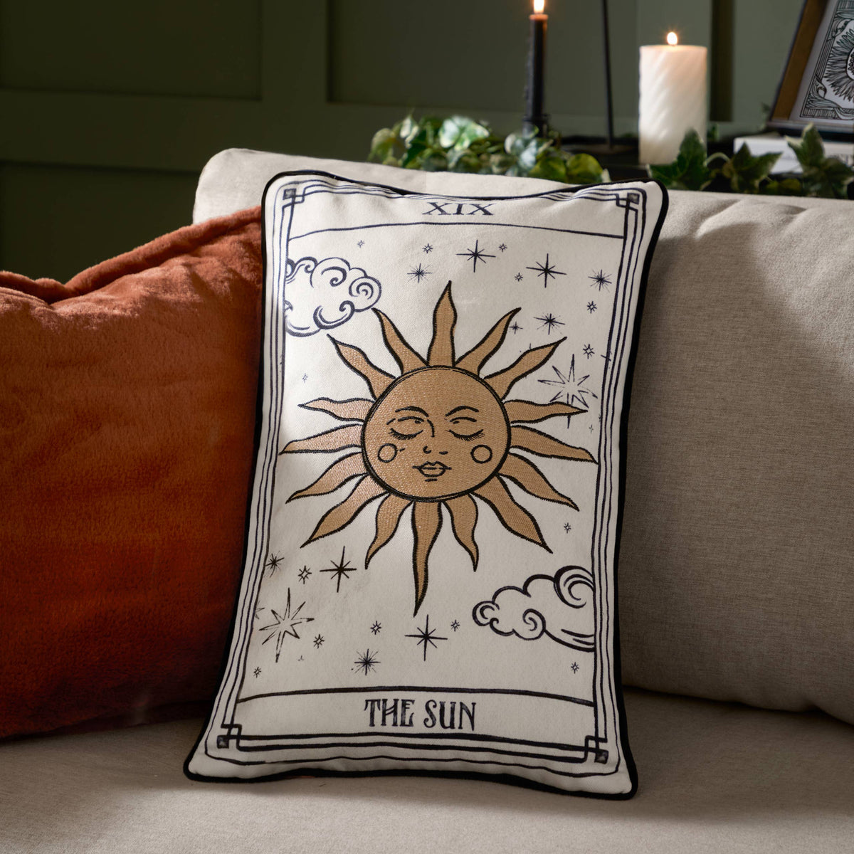 Sun tarot cushion styled on a sofa beside a rust cushion and candles