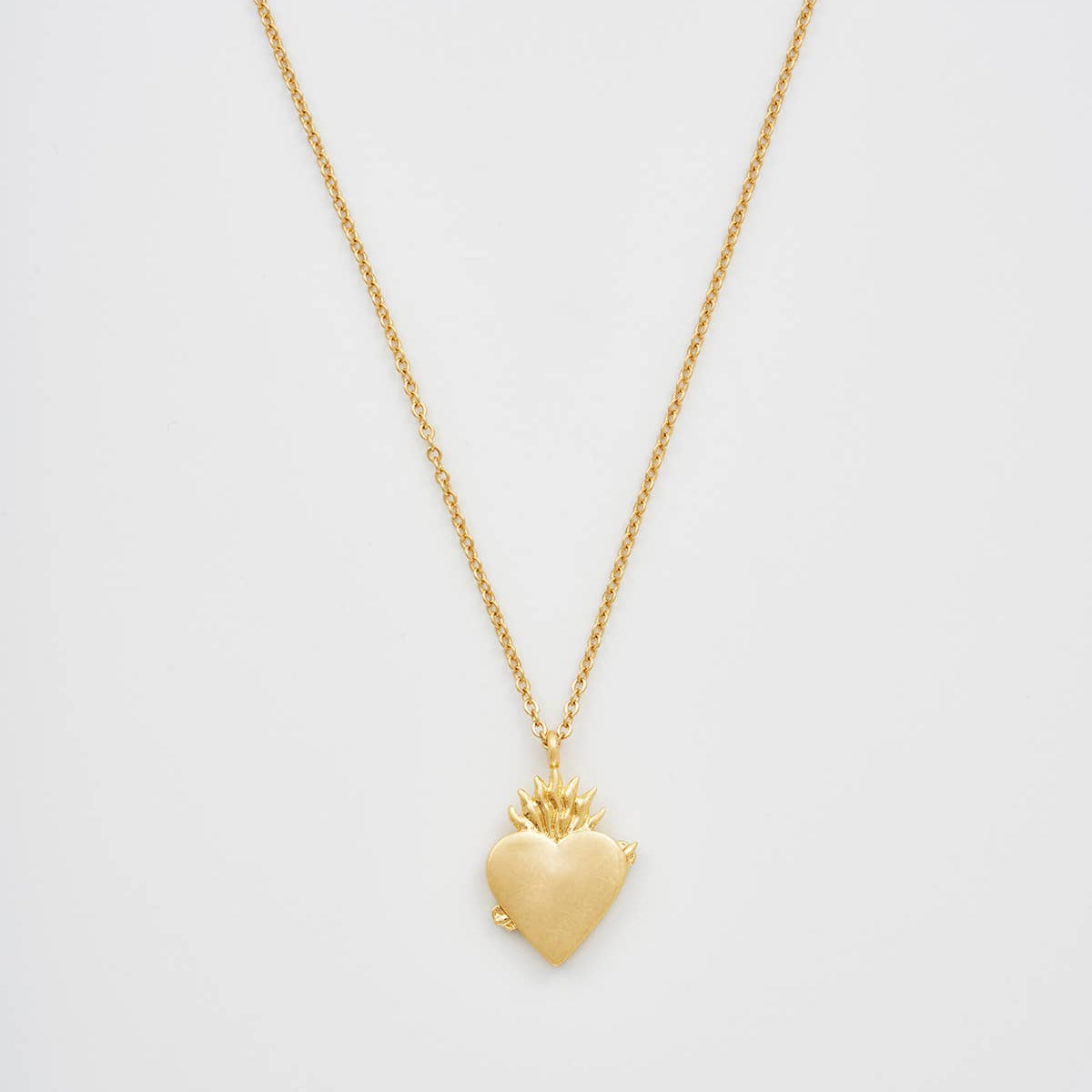 Gold sacred heart necklace pendant on white background.