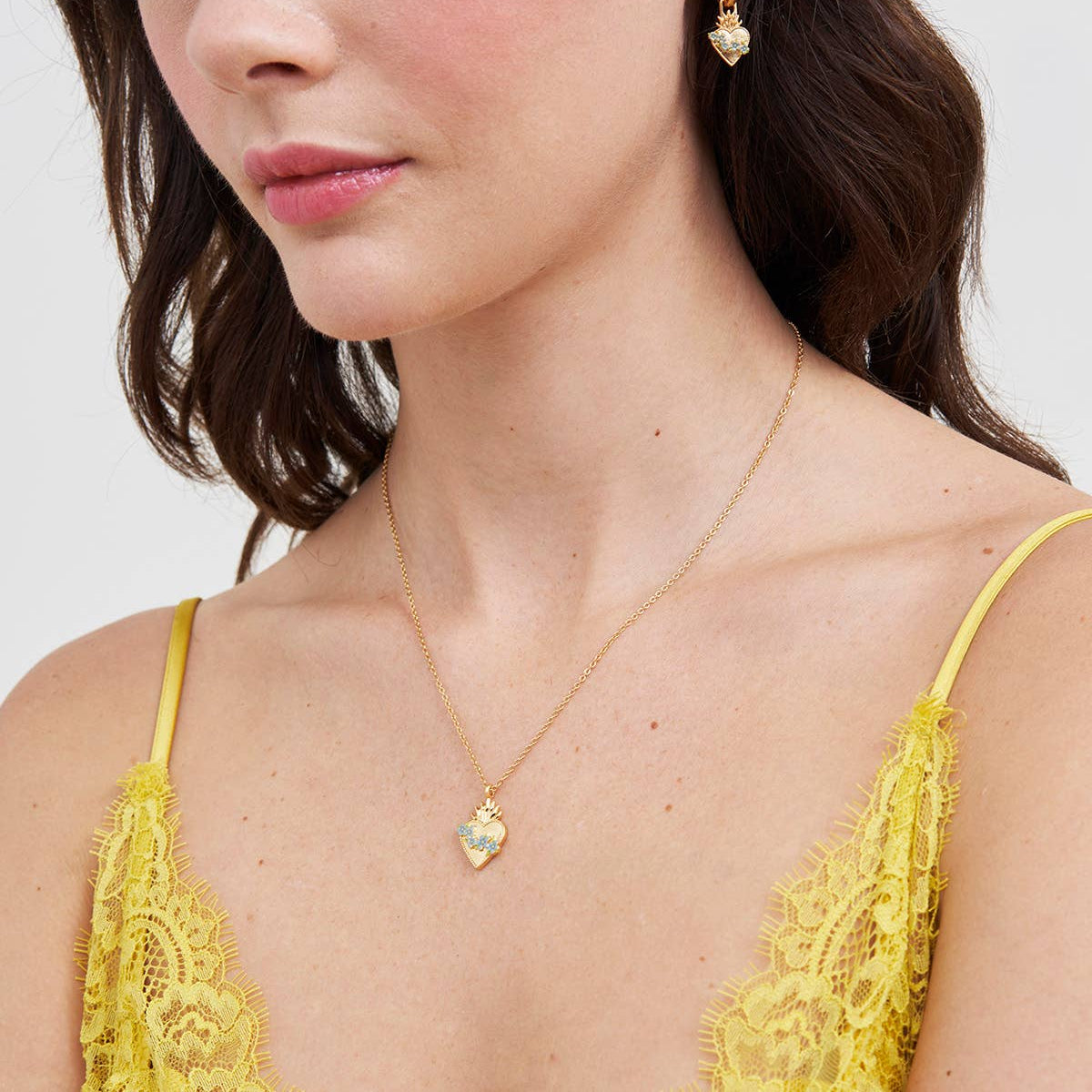 Model wearing gold and blue sacred heart necklace with matching earrings.
