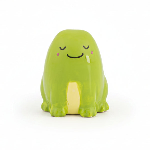 Green ceramic frog token with a sleepy smiling face, front view on white