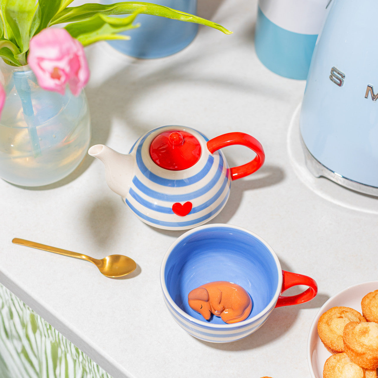 Striped teapot and cup on a kitchen worktop beside pink tulips