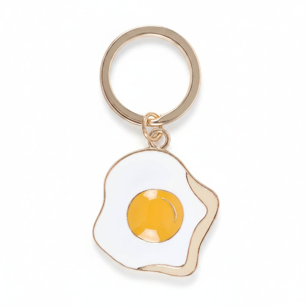 Fried egg enamel charm close-up with gold outline on white background