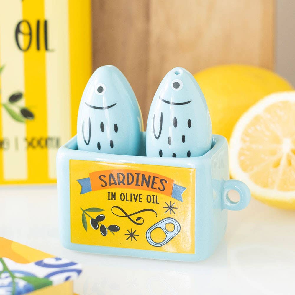 Two sardine shakers on dark surface with lemons and seasoning