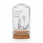 Small glass bottle with cork lid containing floral earrings and a label on a wooden surface.