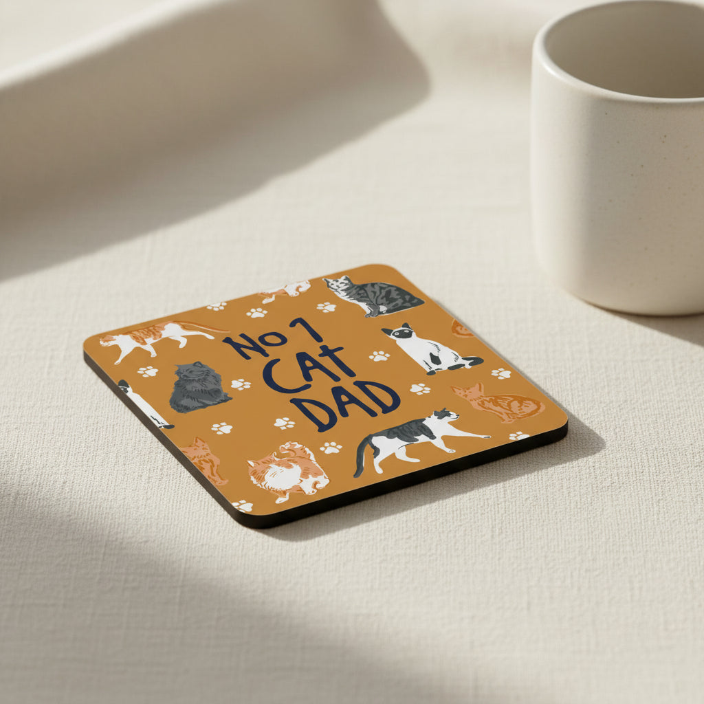 A square coaster with rounded corners featuring a warm brown background decorated with various cartoon cat illustrations and paw prints, with the text 'NO 1 CAT DAD' written in the center.