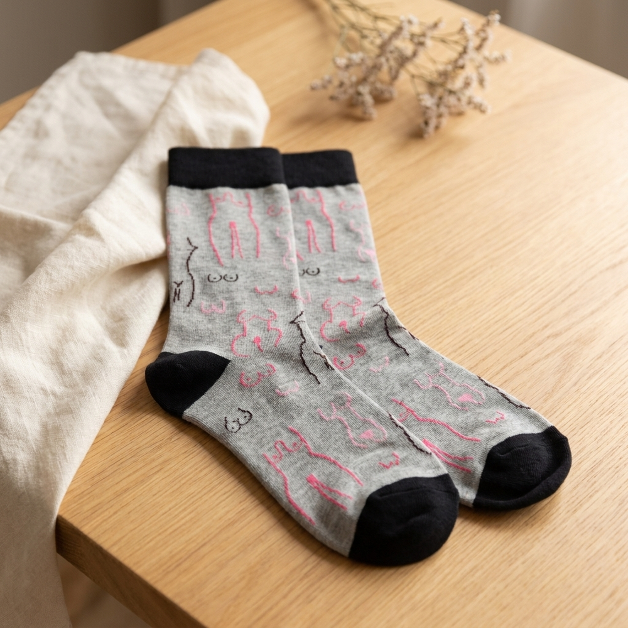 Grey boob print socks styled on warm light wood with cream linen and dried flowers