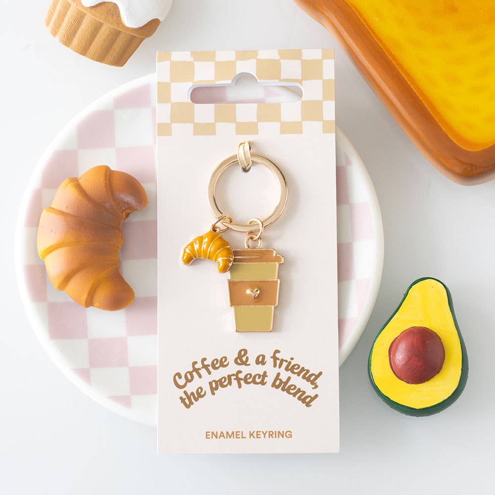 Enamel croissant and coffee cup keyring on packaging card with styled flat lay