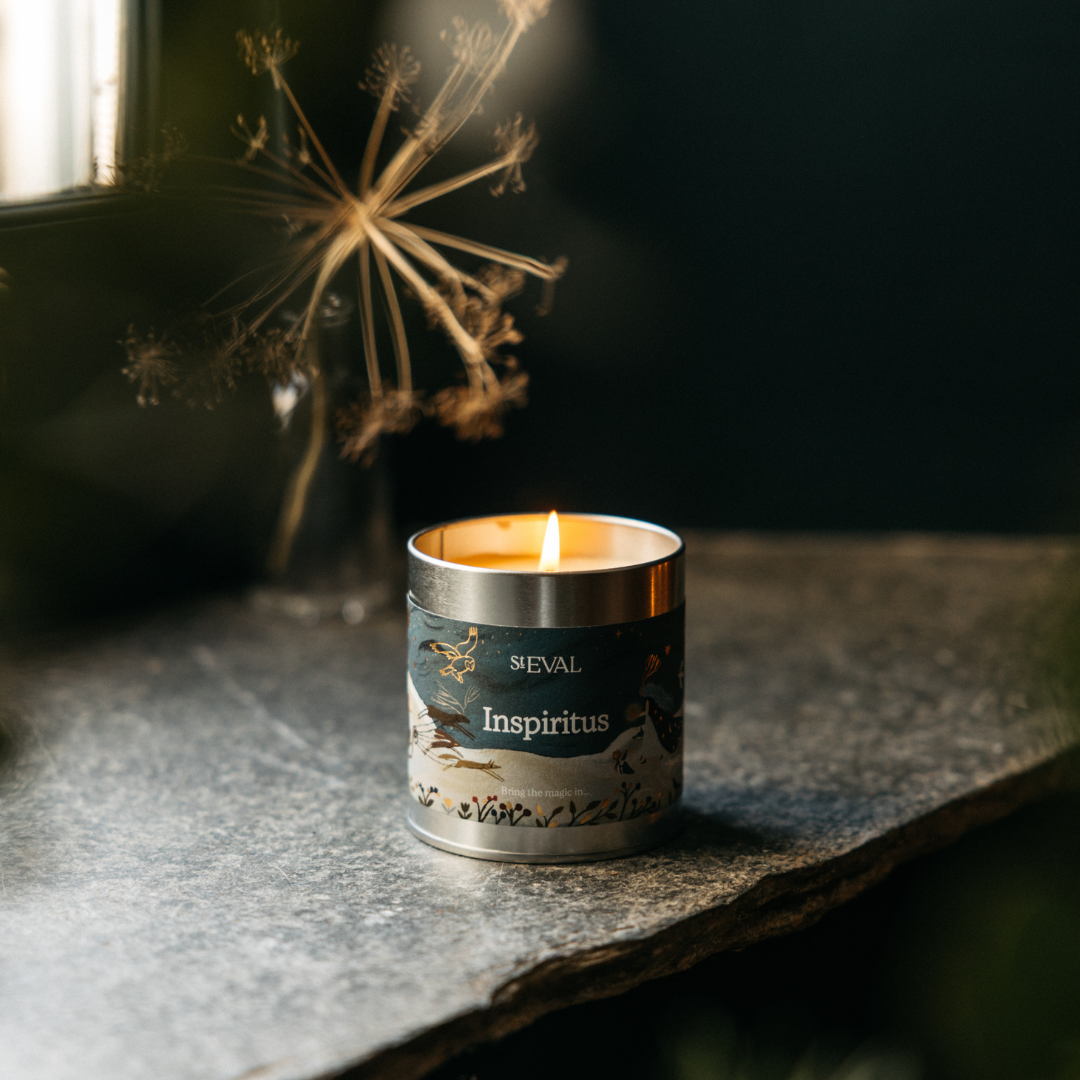 Inspiritus Christmas Tin Candle lit on a dark table with festive lights behind