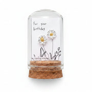 Small glass bottle with floral earrings and a card on a wooden surface