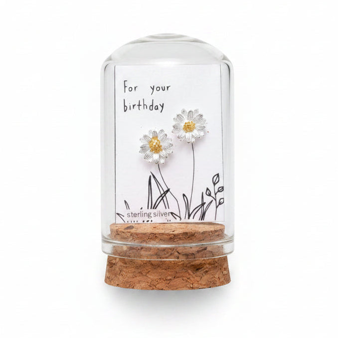 Small glass bottle with floral earrings and a card on a wooden surface