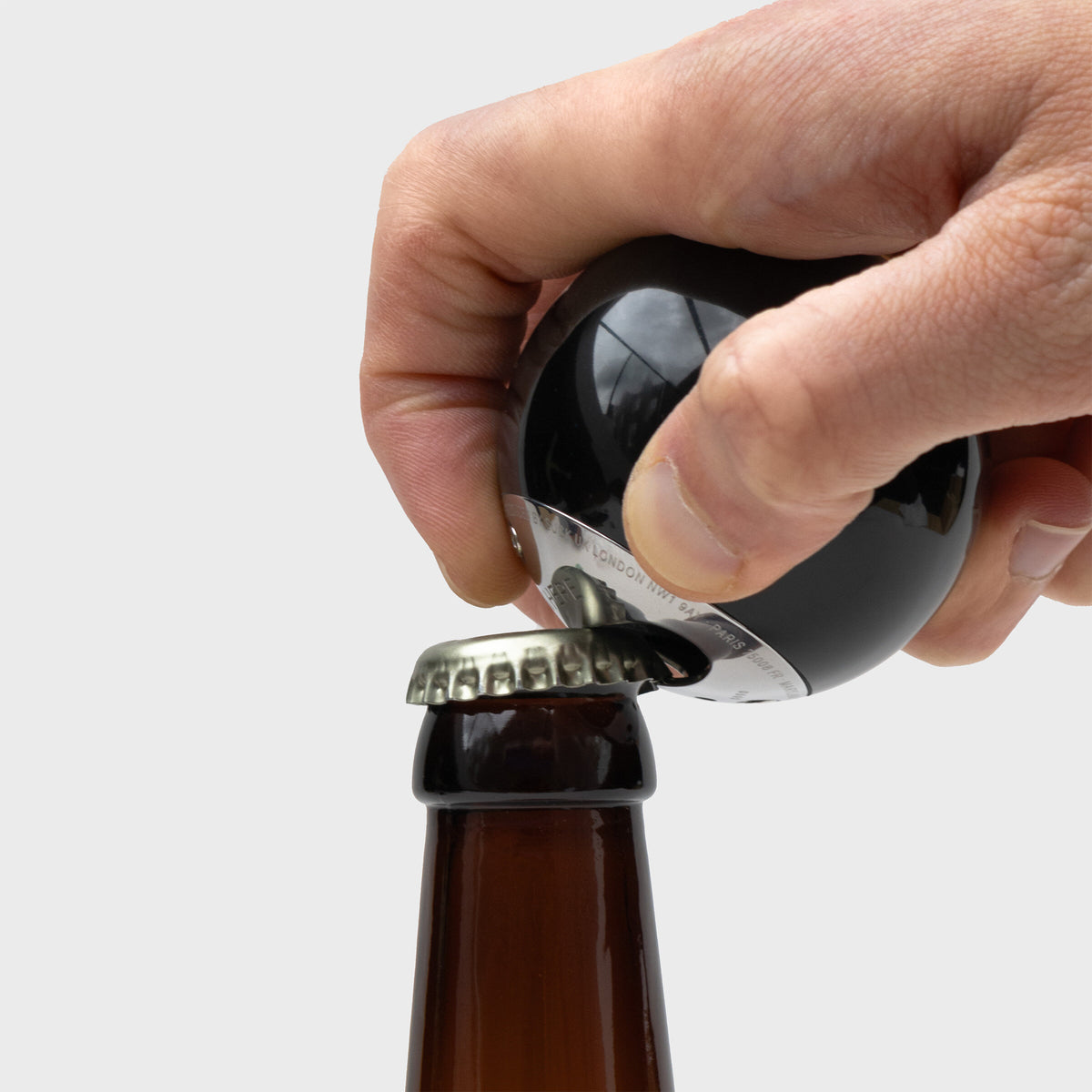 Hand using the 8 ball bottle opener to open a beer bottle