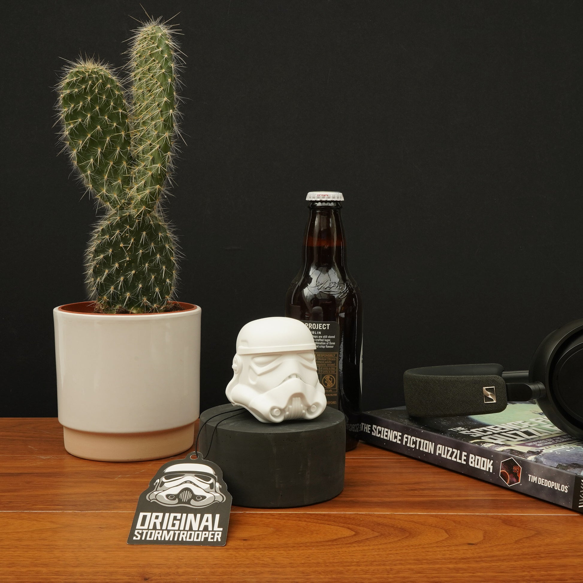 Stormtrooper bottle opener on a desk beside beer bottle, cactus and sci-fi books