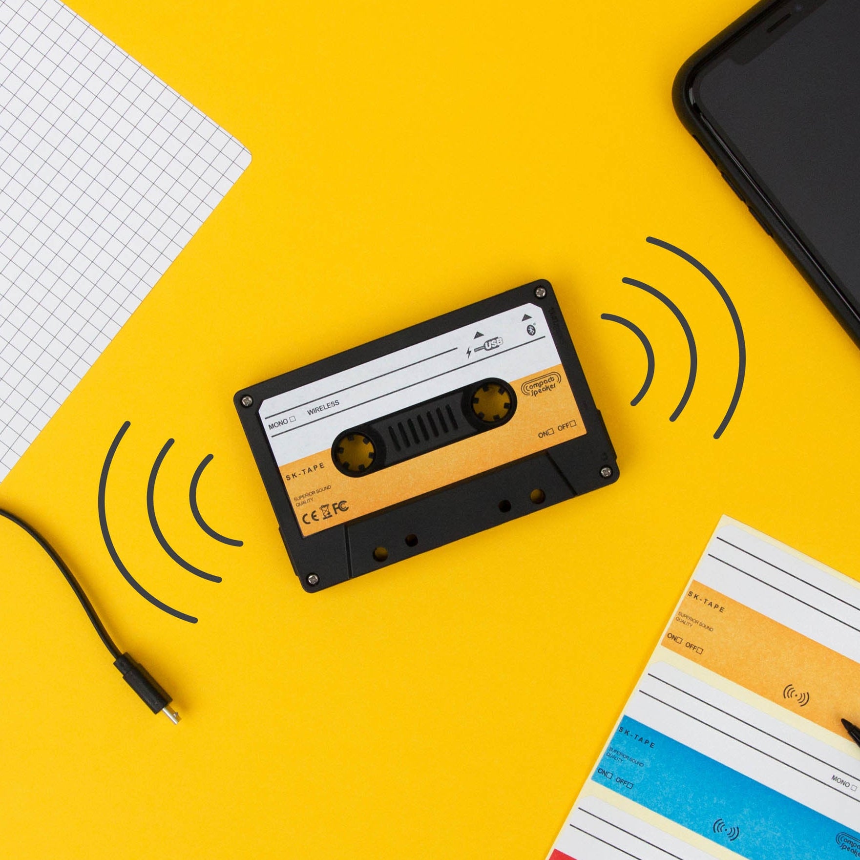 Wireless cassette speaker on yellow background with phone and USB cable