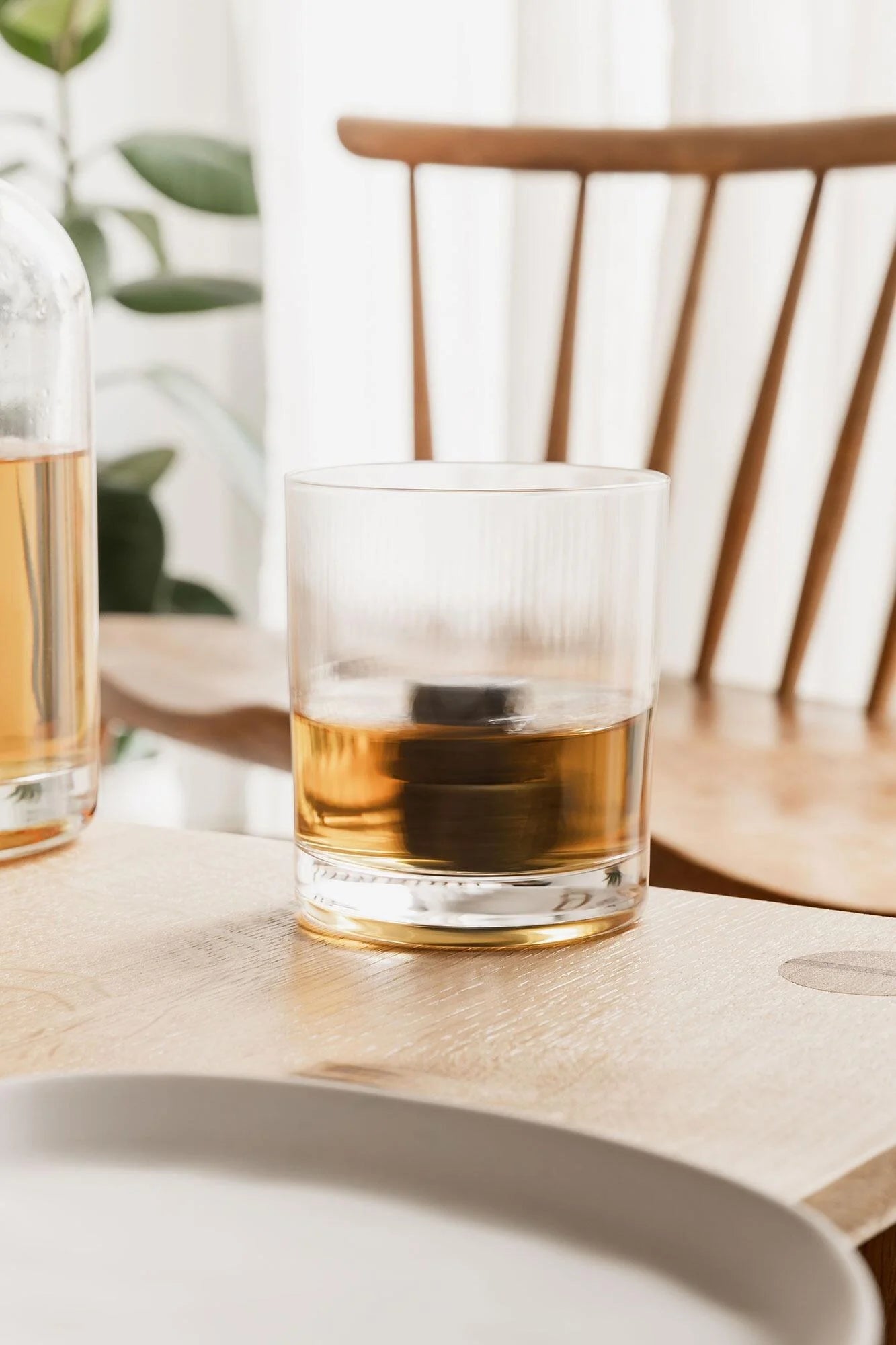 Twisted Whiskey Glass with whisky and stones beside bottle on table.