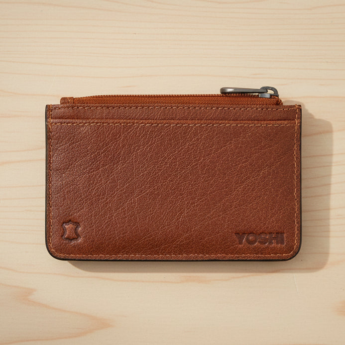 Brown leather zip-top card holder back view with Yoshi branding on wood surface